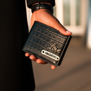 A close-up of a hand holding a black crocodile-textured wallet with a golden “Love” script emblem and a brass nameplate engraved “HIMANSHU.” Customised Wallet for Men 