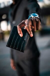 A close-up of a hand holding a black textured wallet embossed with a crocodile pattern. A small label reads “GOLD | BLACK.” Customised Wallet for Men